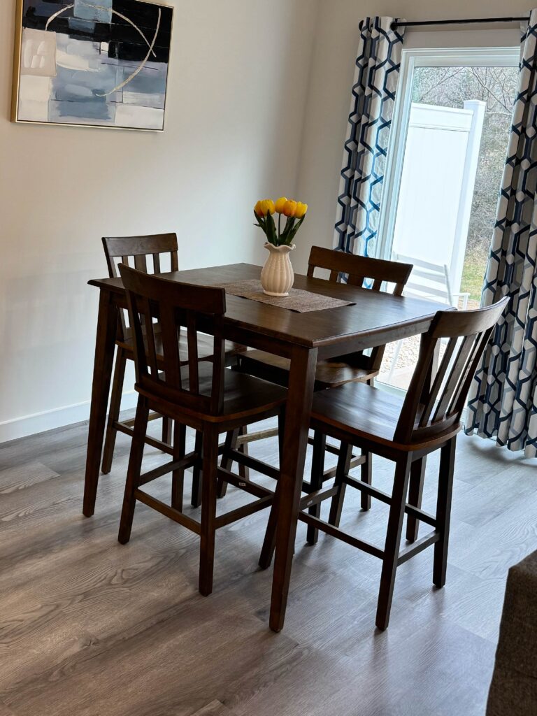 Four-person dining area with a dark wood table, matching chairs, decorative artwork, and access to a private patio.