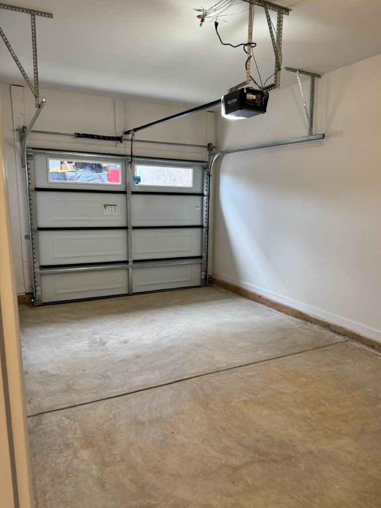 Attached one-car garage with automatic garage door opener, concrete flooring, and overhead storage potential.