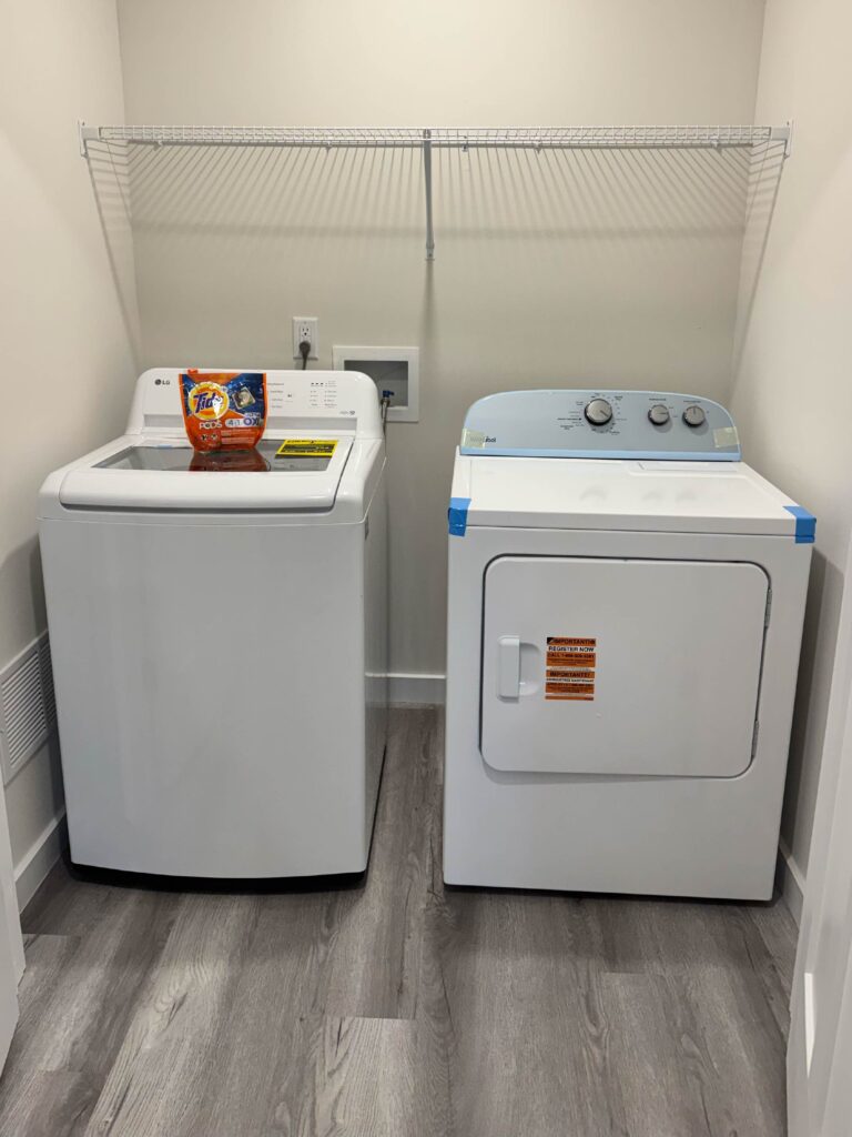 Dedicated laundry room featuring a full-size LG top-load washer and dryer, overhead storage shelving, and luxury vinyl plank flooring.