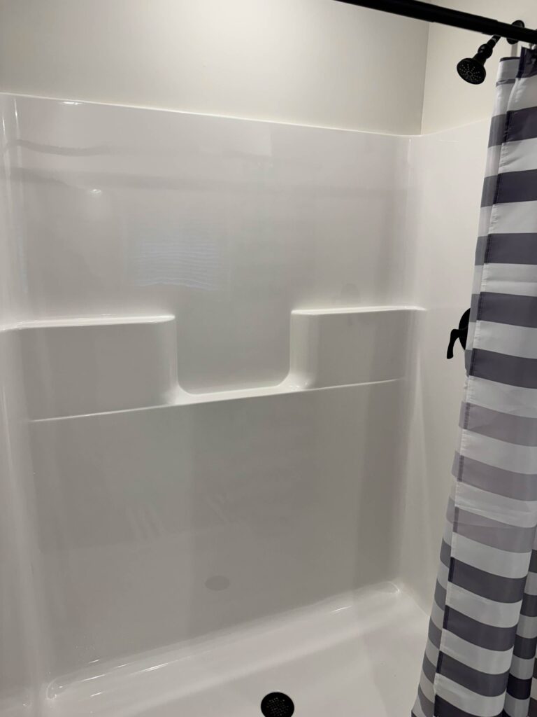 Clean walk-in shower featuring a white surround with built-in shelving, matte black fixtures, and a striped shower curtain in a bright modern bathroom.
