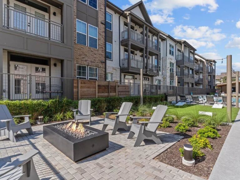 Outdoor community courtyard at Lenox Grand Apartments in Austin, Texas featuring a modern fire pit, Adirondack seating, landscaped grounds, luxury apartment buildings, and resort style outdoor gathering spaces.