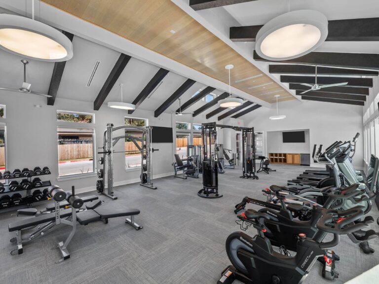 Modern fitness center at Lenox Grand Apartments in Austin, Texas featuring cardio equipment, free weights, strength training stations, spin bikes, and spacious high ceiling design.