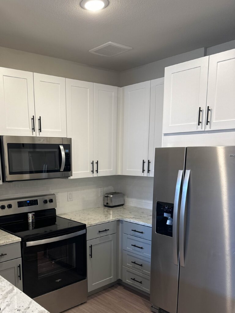 Modern kitchen at Lenox Grand Apartments in Austin, Texas featuring stainless steel appliances, granite countertops, shaker style cabinetry, built in microwave, electric range, and spacious storage.