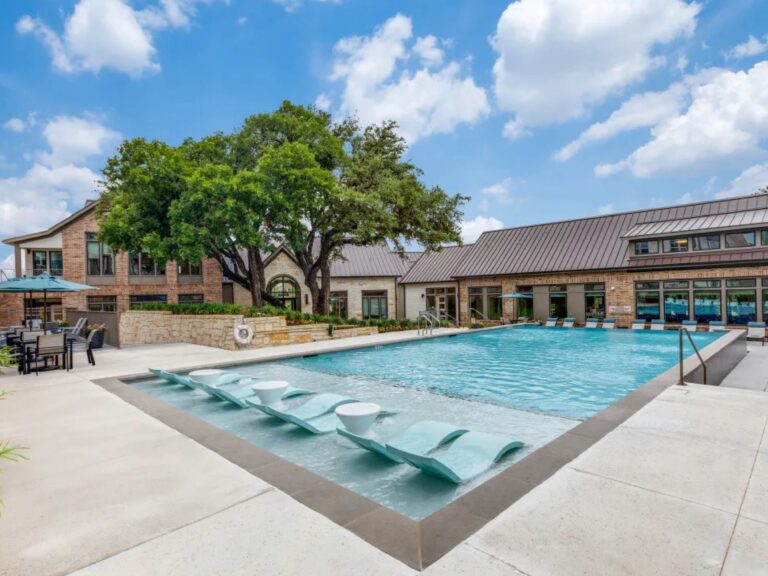 Resort style swimming pool at Lenox Grand Apartments in Austin, Texas featuring expansive water views, in pool lounge chairs, sun deck seating, luxury clubhouse amenities, and professionally landscaped grounds.