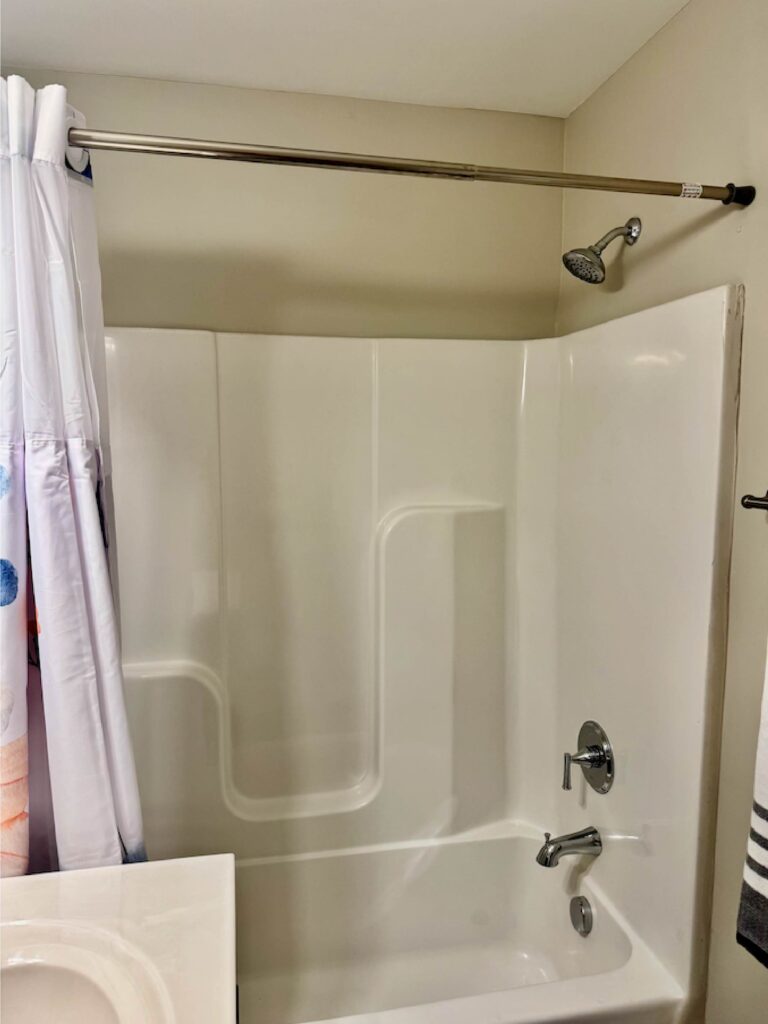 Standard bathroom with a full-size tub and shower combination, white surround walls, chrome fixtures, shower curtain, and towel rack in a furnished apartment at Lofts at Rose Monte in Nashville.