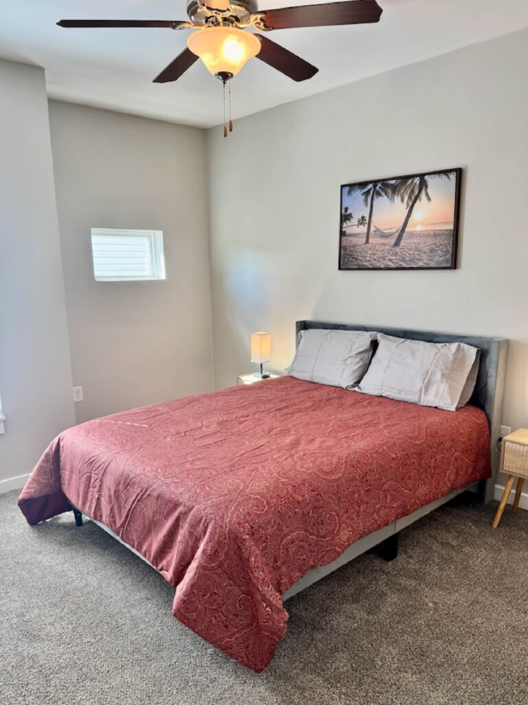 Spacious primary bedroom featuring a king-size bed, plush carpeting, bedside tables with lamps, ceiling fan, and calming coastal-inspired décor.