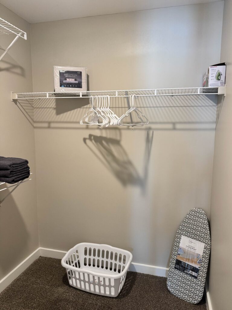 Spacious walk-in closet featuring hanging space, shelving, extra linens, clothes hangers, an ironing board, steam iron, and a laundry basket for guest convenience.