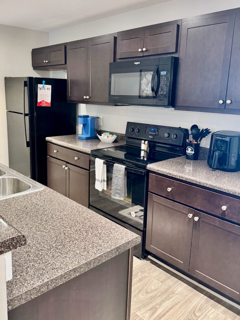 Modern kitchen featuring full-size black appliances, spacious cabinetry, ample countertop space, microwave, coffee maker, air fryer, and a large island with sink.