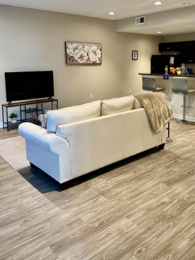 Spacious open concept living area featuring a comfortable sofa, flat-screen television, breakfast bar seating, and a fully equipped kitchen with modern finishes.