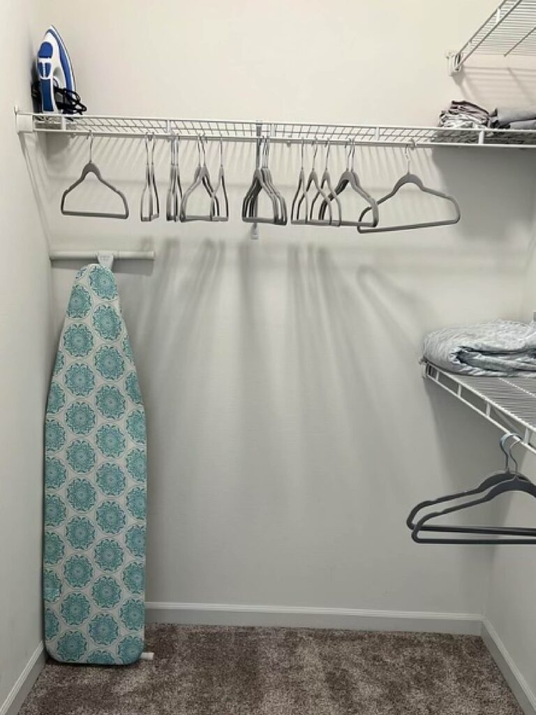 Walk in closet with shelving, hanging space, ironing board, extra linens, and clothing hangers.
