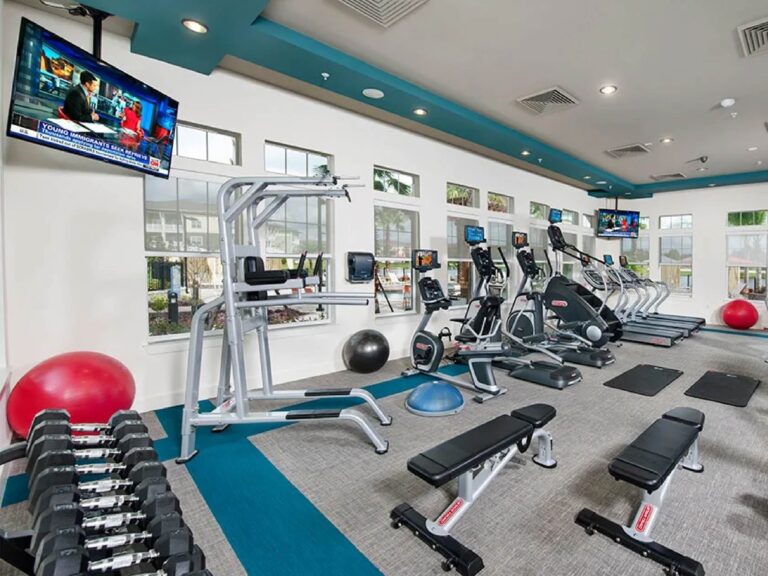 Modern fitness center with cardio machines, free weights, workout benches, and mounted televisions.