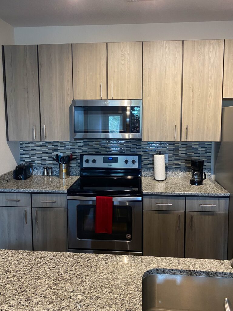 Modern kitchen with stainless steel appliances, wood cabinetry, granite countertops, and mosaic tile backsplash.