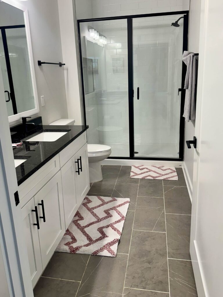 Modern bathroom featuring a double vanity with quartz countertops, black fixtures, framed mirrors, spacious walk-in shower with glass enclosure, and contemporary tile flooring.