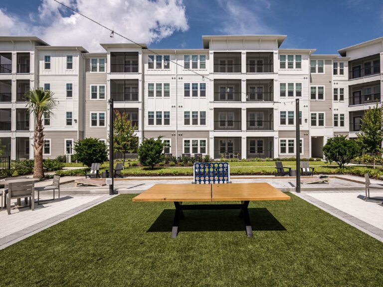 Outdoor community game lawn featuring a ping pong table, oversized Connect Four game, lounge seating, and landscaped courtyard.