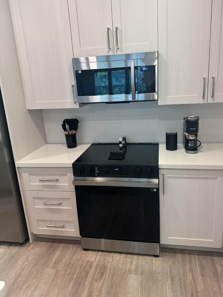 Modern kitchen with stainless steel appliances, white cabinetry, subway tile backsplash, and fully furnished cooking essentials.