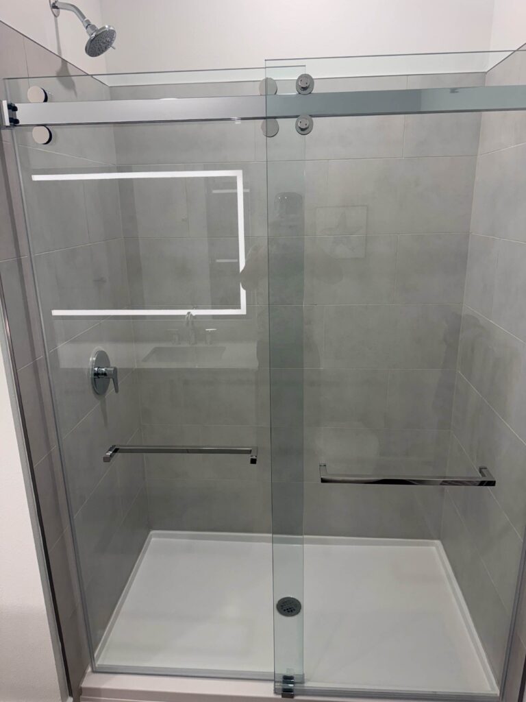 Modern walk-in shower with frameless sliding glass doors, large gray tile walls, and contemporary fixtures.