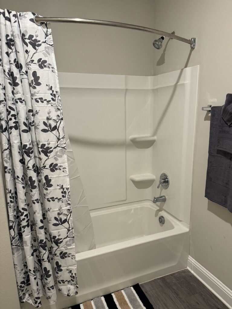 Clean full bathroom featuring a tub and shower combination, curved shower rod, decorative shower curtain, and fresh towels.