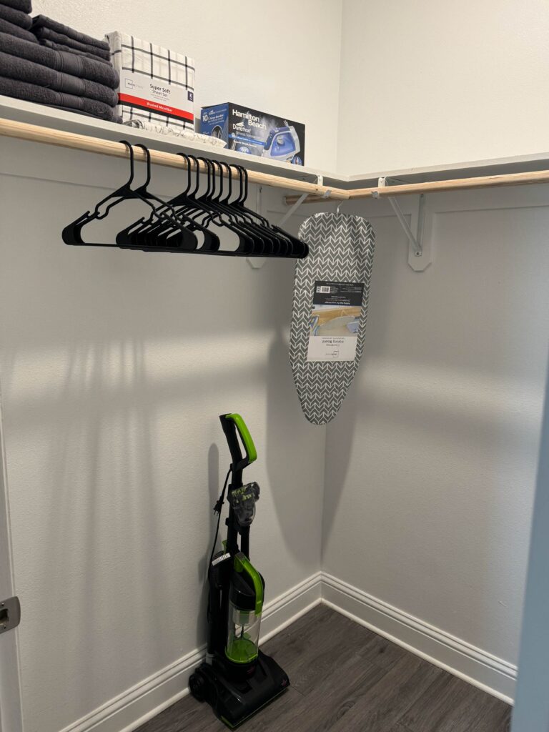 Walk-in closet featuring ample hanging space, storage shelving, extra linens, hangers, ironing supplies, and a vacuum cleaner.
