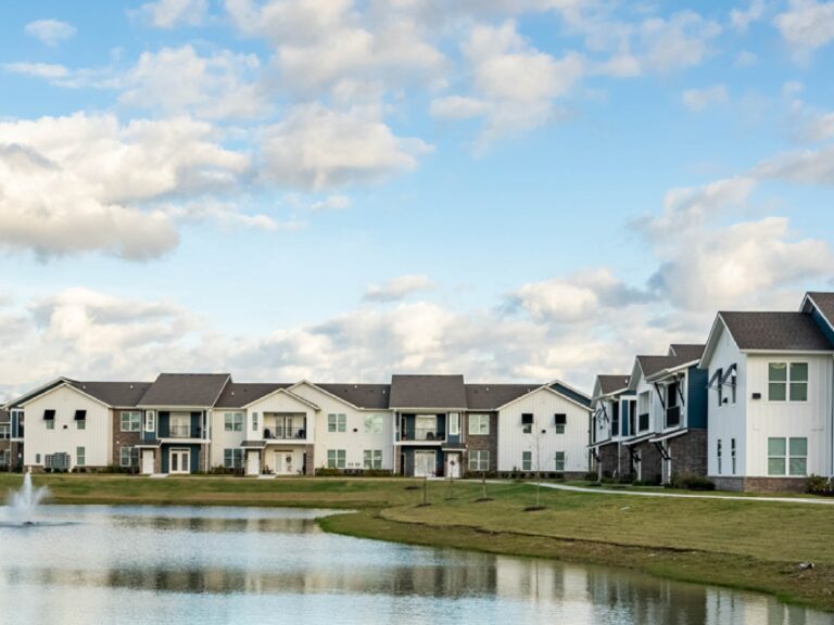 Lakeside view at Oasis at Southpark featuring modern apartment buildings, landscaped grounds, walking areas, and a scenic community pond with fountain.