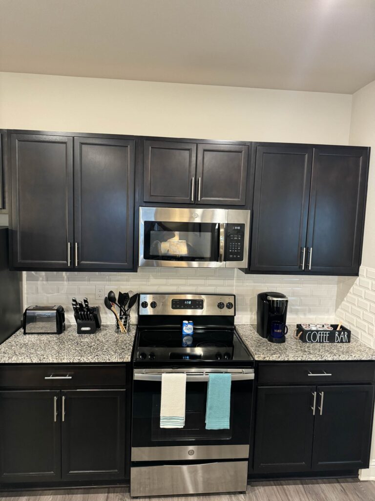 Modern kitchen featuring granite countertops, dark wood cabinetry, stainless steel appliances, and a dedicated coffee station.