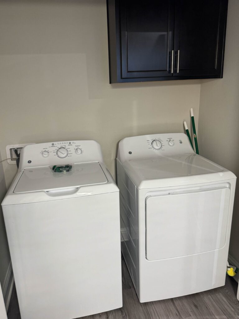 Dedicated laundry room featuring a full-size washer and dryer, overhead storage cabinet, and convenient in-unit laundry facilities.