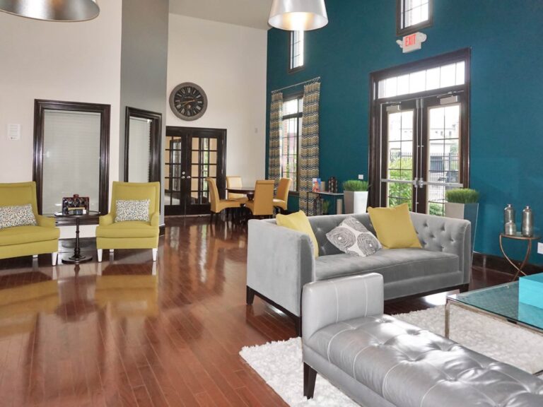 Modern clubhouse lounge with high ceilings, hardwood floors, stylish seating, and large windows with natural light.