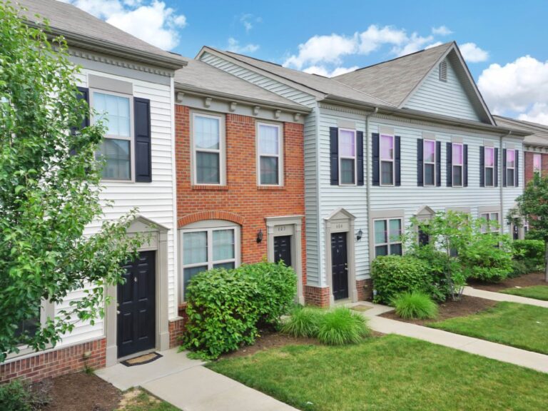 Row of modern townhome style residences with brick accents, landscaped walkways, and manicured green spaces.