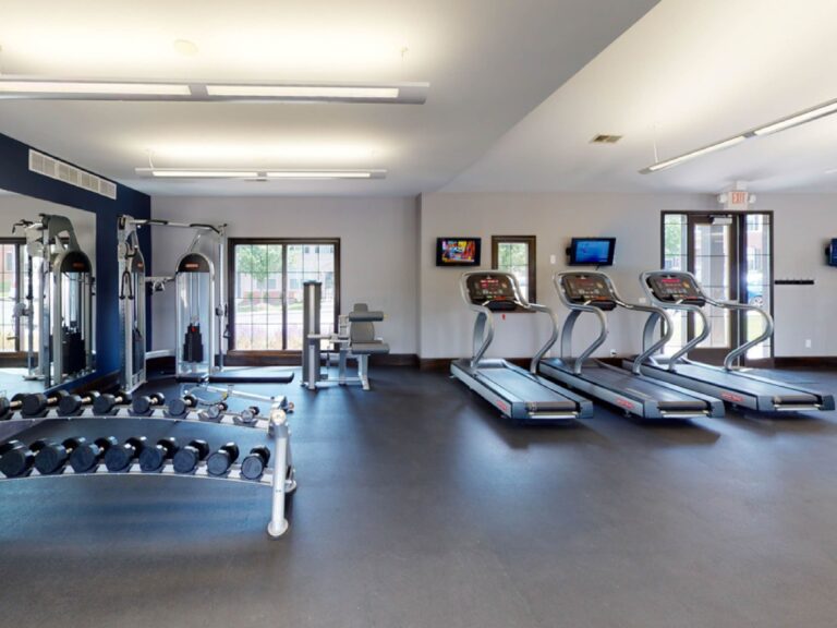 Modern fitness center with treadmills, free weights, strength training equipment, and mounted televisions.