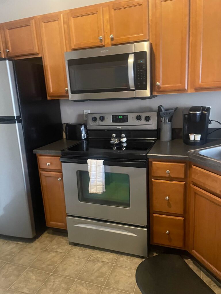 Modern kitchen with stainless steel appliances, wood cabinetry, coffee maker, and fully equipped cooking space.