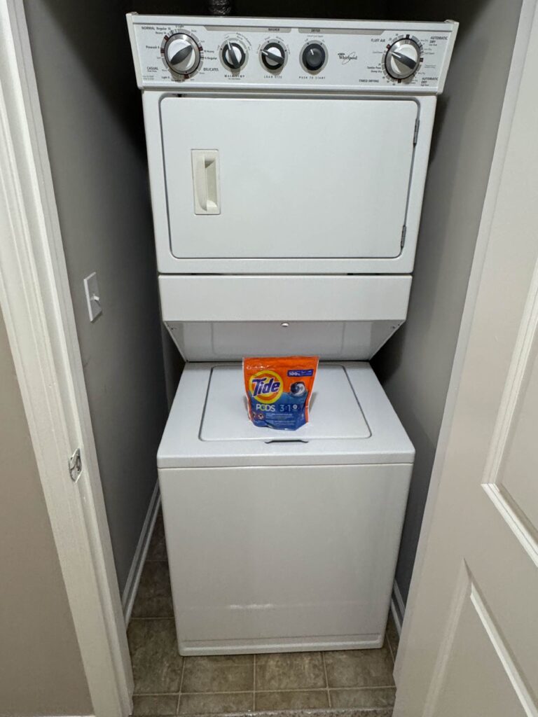 Stacked washer and dryer unit with complimentary Tide Pods in a dedicated laundry closet.