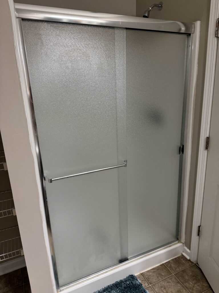 Frosted glass walk in shower with sliding doors and chrome fixtures in a modern bathroom.