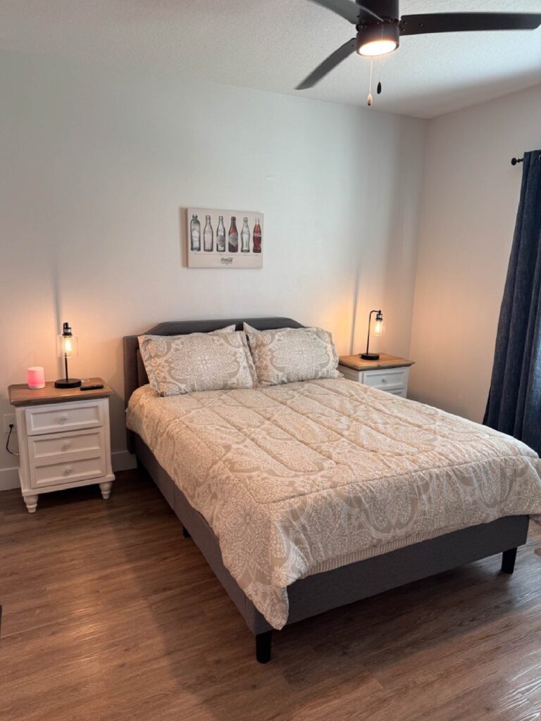 Modern furnished bedroom at Sorrento Apartments with queen bed, wood style flooring, ceiling fan, and bedside lighting