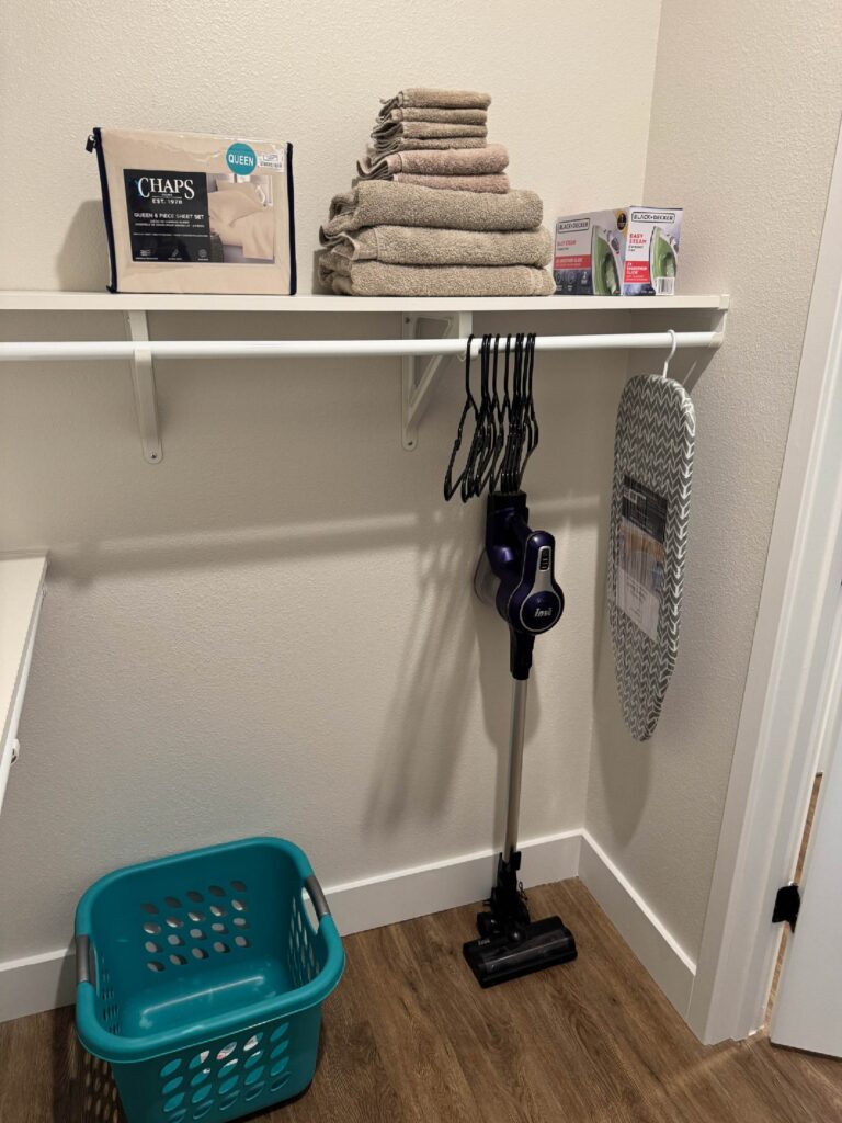 Organized walk in storage closet at Sorrento Apartments with linens, towels, vacuum, ironing board, and guest laundry essentials