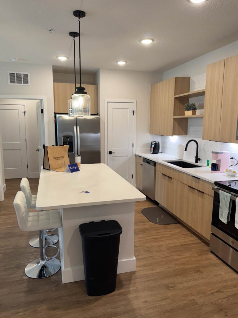 Modern kitchen at Sorrento Apartments with oversized island, stainless steel appliances, pendant lighting, and furnished dining seating