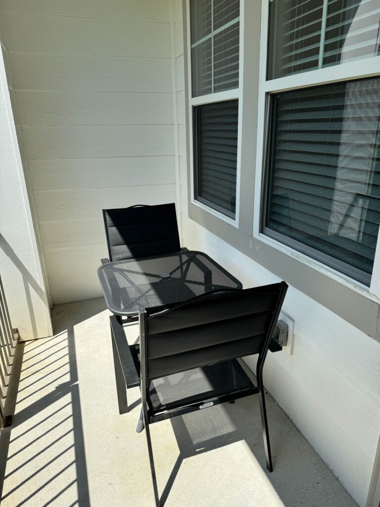 Private balcony at Tapestry Bocage featuring a bistro table with two chairs, outdoor seating, and views from an upper-floor apartment.