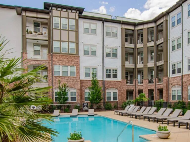 Luxury apartment community at Tapestry Bocage featuring a resort style swimming pool, sun loungers, landscaped courtyard, and multi story residential buildings.