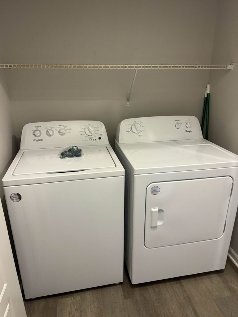 In unit laundry room at Tapestry Bocage featuring full size Whirlpool washer and dryer with dedicated storage space.