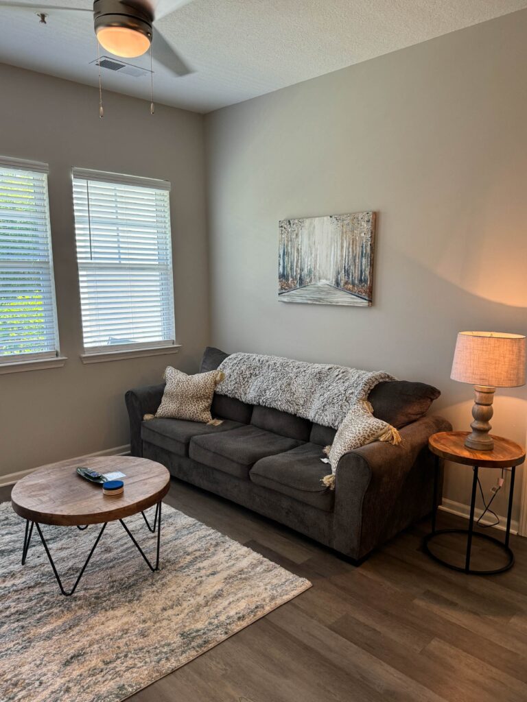 Living room at Tapestry Bocage featuring a comfortable sofa, accent pillows, coffee table, area rug, large windows, and warm ambient lighting.