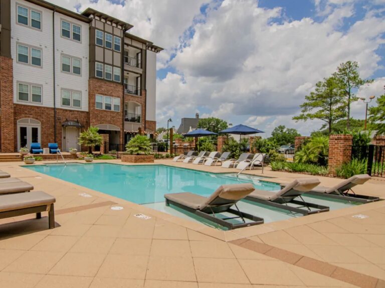 Resort style swimming pool at Tapestry Bocage featuring in-water lounge chairs, expansive sun deck seating, landscaped surroundings, and luxury apartment buildings.