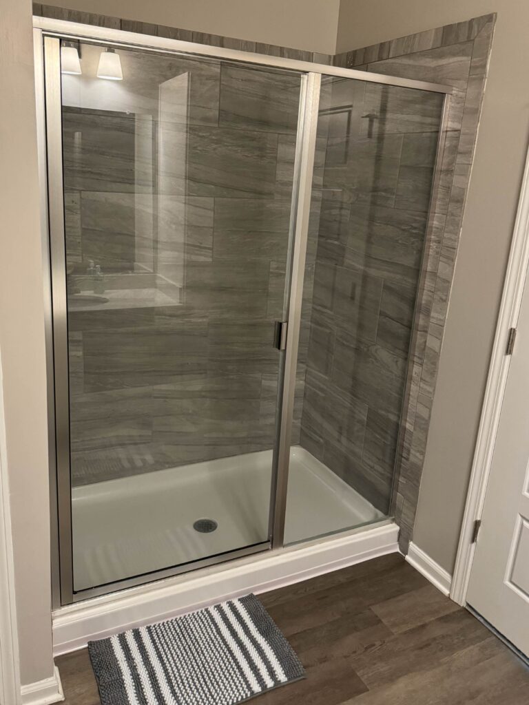 Modern walk in shower at Tapestry Bocage featuring floor to ceiling tile surround, glass sliding doors, and upscale finishes.