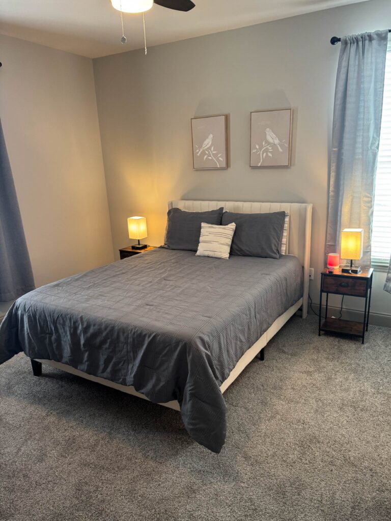 Modern furnished bedroom with gray bedding, carpeted flooring, bedside lamps, and contemporary décor at The Hub in Bowling Green, Kentucky.