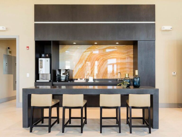 Modern clubhouse coffee bar with seating, dark wood finishes, beverage station, and decorative stone accent wall.