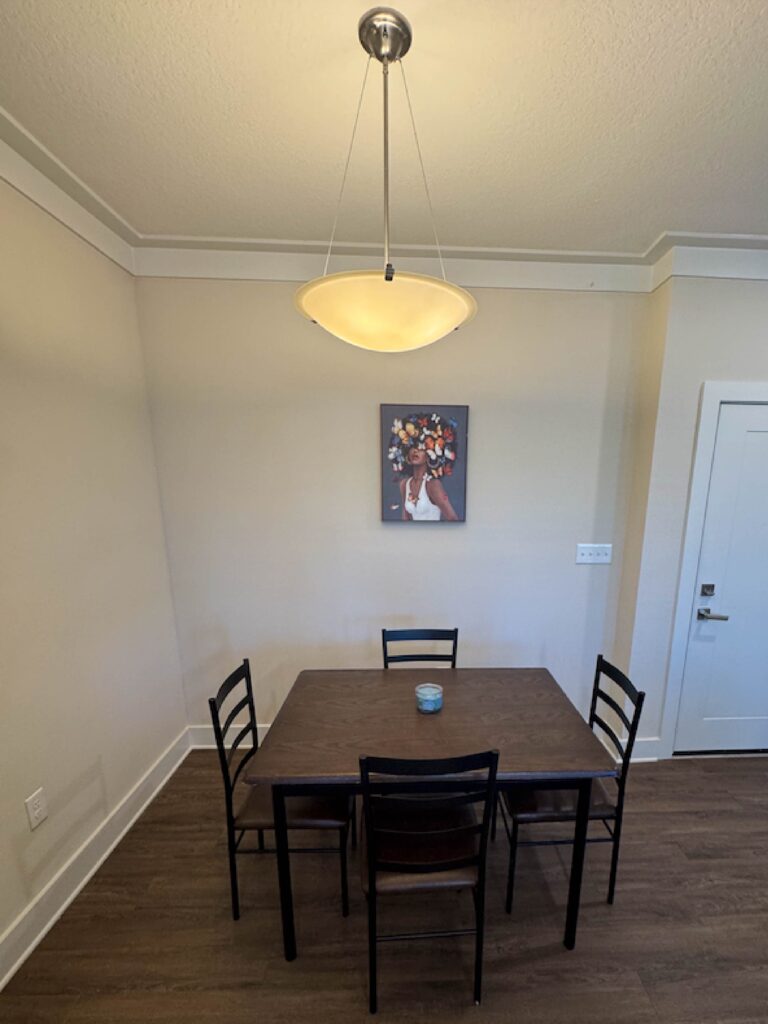 Dining area with a four person table, modern pendant light, framed artwork, and dark wood flooring.