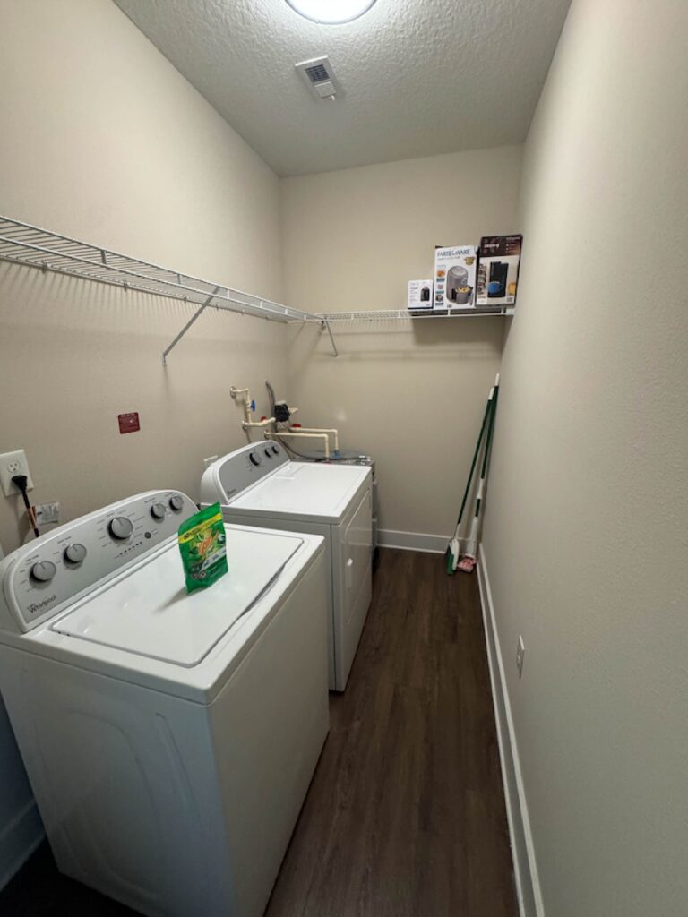 Dedicated laundry room with full-size washer and dryer, shelving, and wood-style flooring.