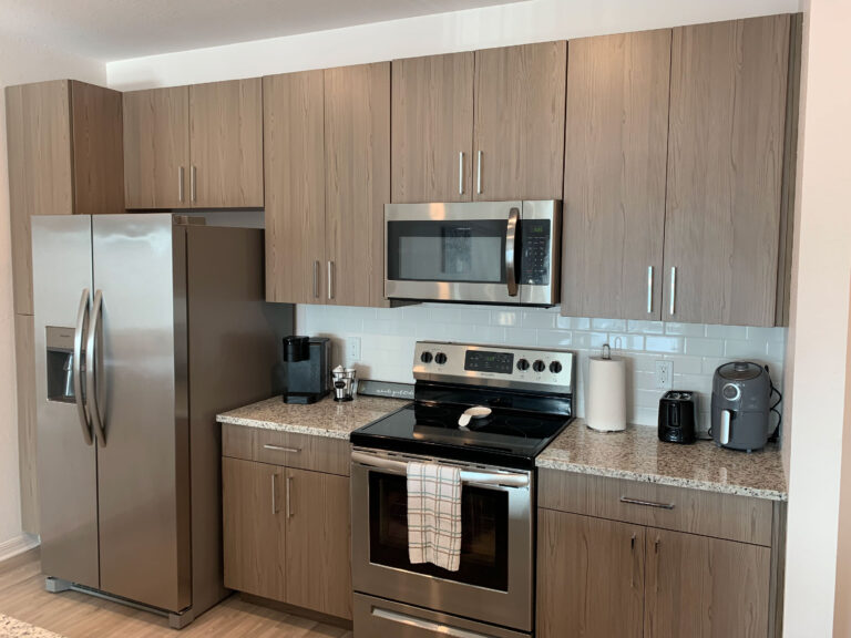 This private balcony at V2 Apartments features outdoor seating and relaxing lakefront views with a decorative fountain, providing extended stay guests and corporate travelers with a comfortable outdoor space to unwind and enjoy the Southwest Florida atmosphere.