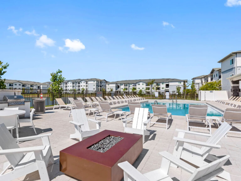 Outdoor resort style pool deck at V2 Apartments in Fort Myers featuring lounge chairs, fire pit seating, grilling area, and modern apartment surroundings.