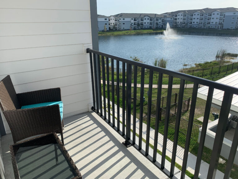 Private balcony at V2 Apartments in Fort Myers overlooking a scenic lake with fountain views and outdoor seating.
