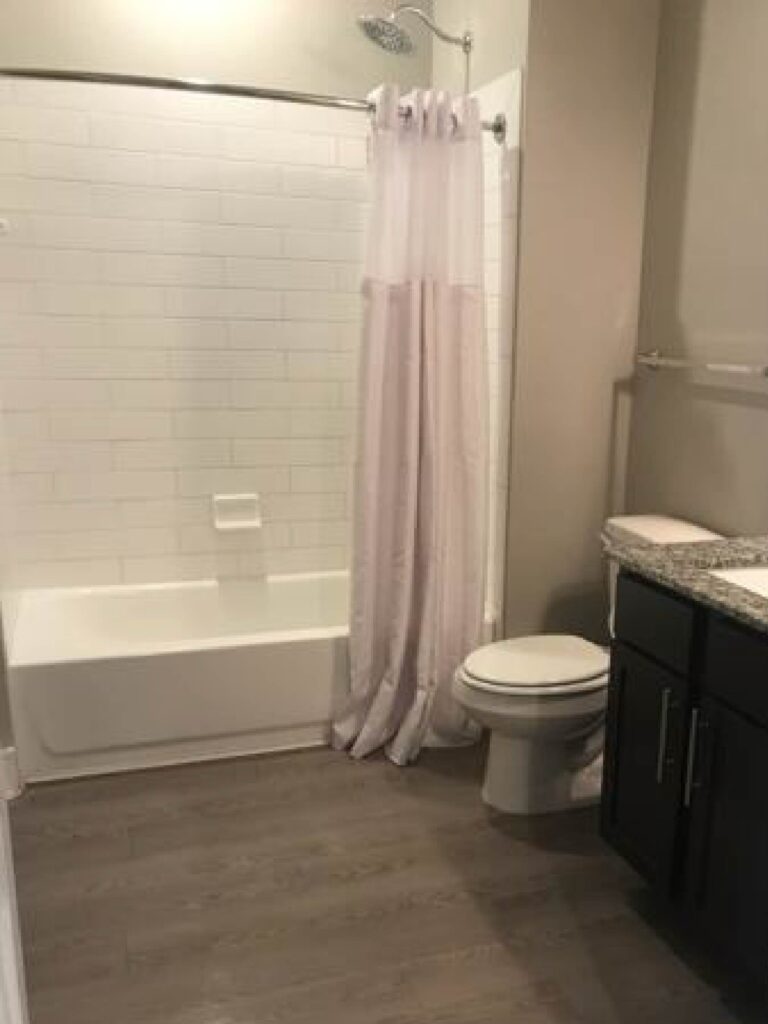 Modern bathroom at Vale Apartments featuring a granite vanity countertop, contemporary cabinetry, full-size bathtub and shower combination, tile surround, and spacious layout.
