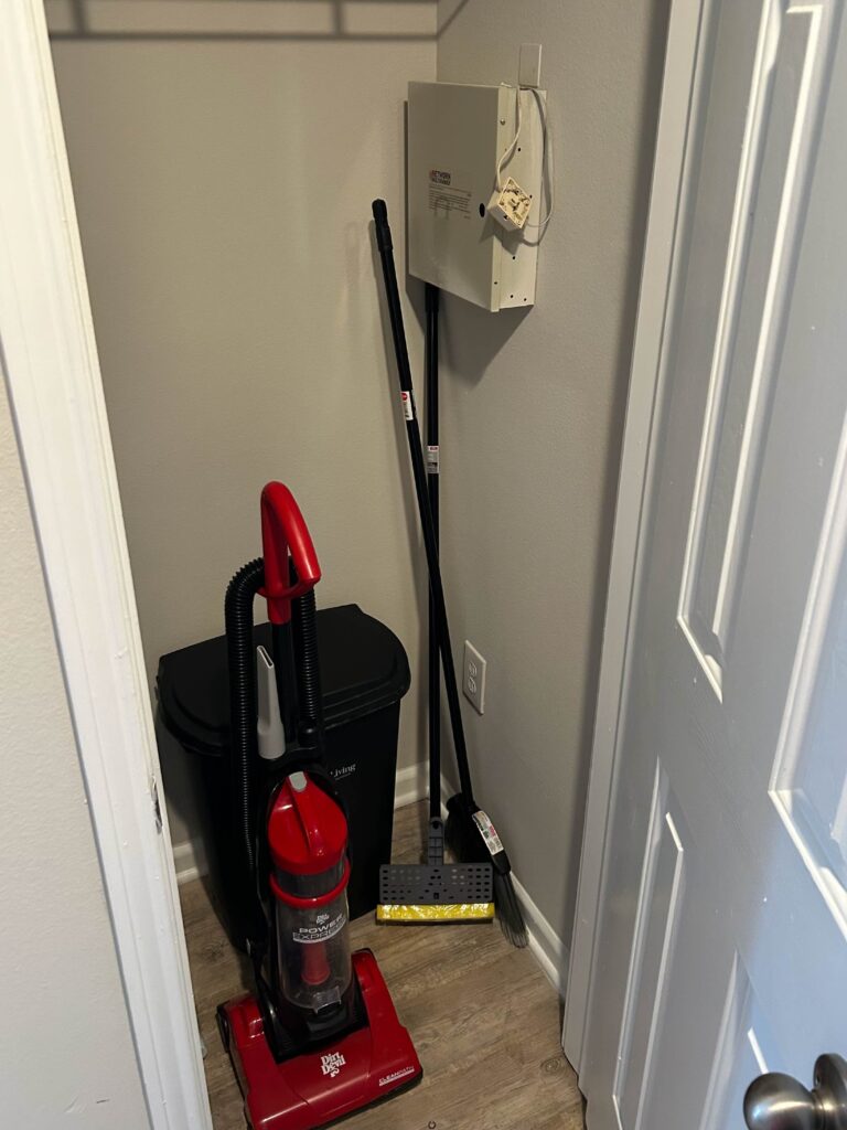 Utility and storage closet at Vista Commons in Columbia, South Carolina, equipped with a vacuum cleaner, broom, dustpan, waste bin, and additional storage space.
