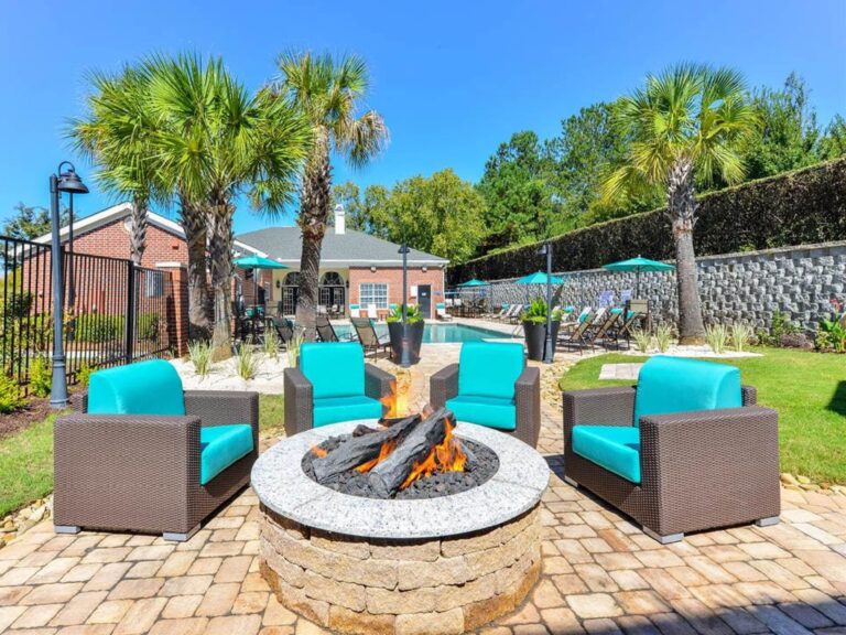 Outdoor community fire pit at Vista Commons in Columbia, South Carolina, surrounded by comfortable lounge seating, palm trees, landscaped grounds, and resort-style pool amenities.